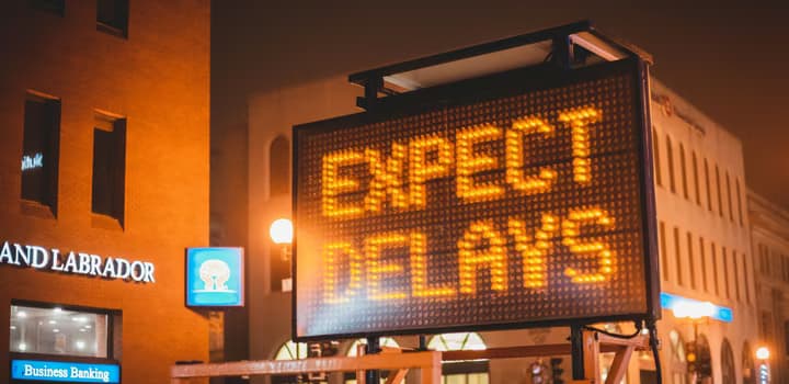 Illuminated "Expect Delays" sign in city streets at night, cautioning drivers.