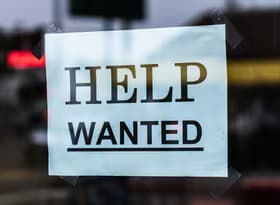 Close-up of a Help Wanted sign taped to a glass window in a storefront.