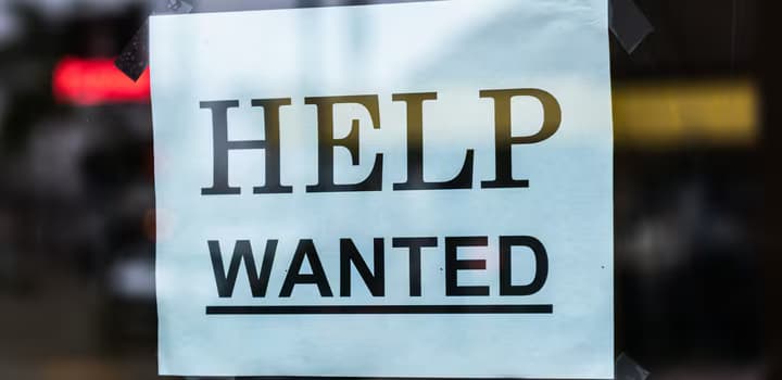 Close-up of a Help Wanted sign taped to a glass window in a storefront.