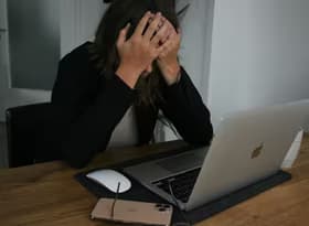 A woman covering her face while looking at a laptop