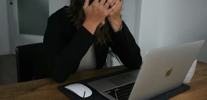 A woman covering her face while looking at a laptop