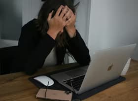 A woman covering her face while looking at a laptop