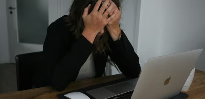 A woman covering her face while looking at a laptop